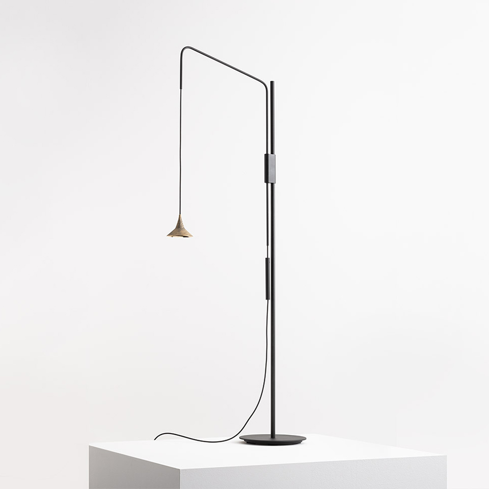 Lampada da terra Artemide Unterlinden: alto fusto nero con braccio regolabile, piccolo paralume conico in ottone, base circolare su piedistallo bianco