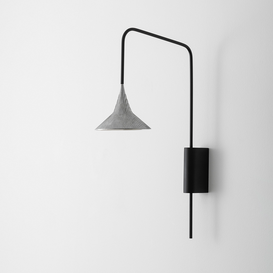 Lampada da parete Artemide Unterlinden Outdoor: braccio orientabile nero con supporto cilindrico a parete e paralume conico testurizzato argento rivolto verso il basso