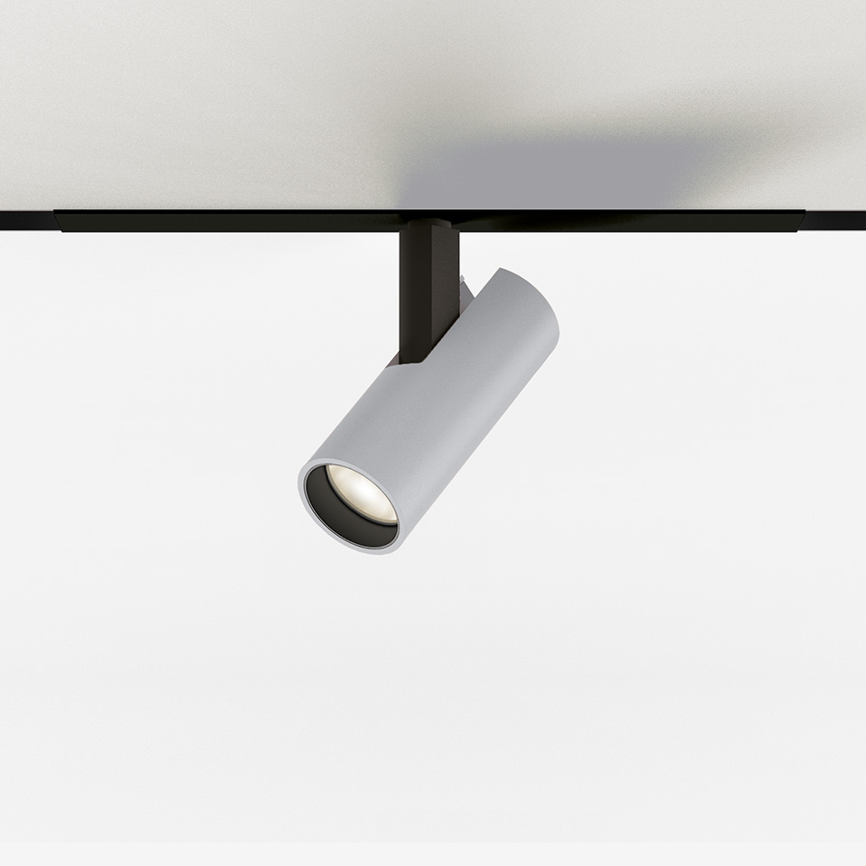 Faretto da binario Artemide Vector Magnetic, corpo cilindrico bianco inclinato, montato su binario magnetico nero, con LED integrato.