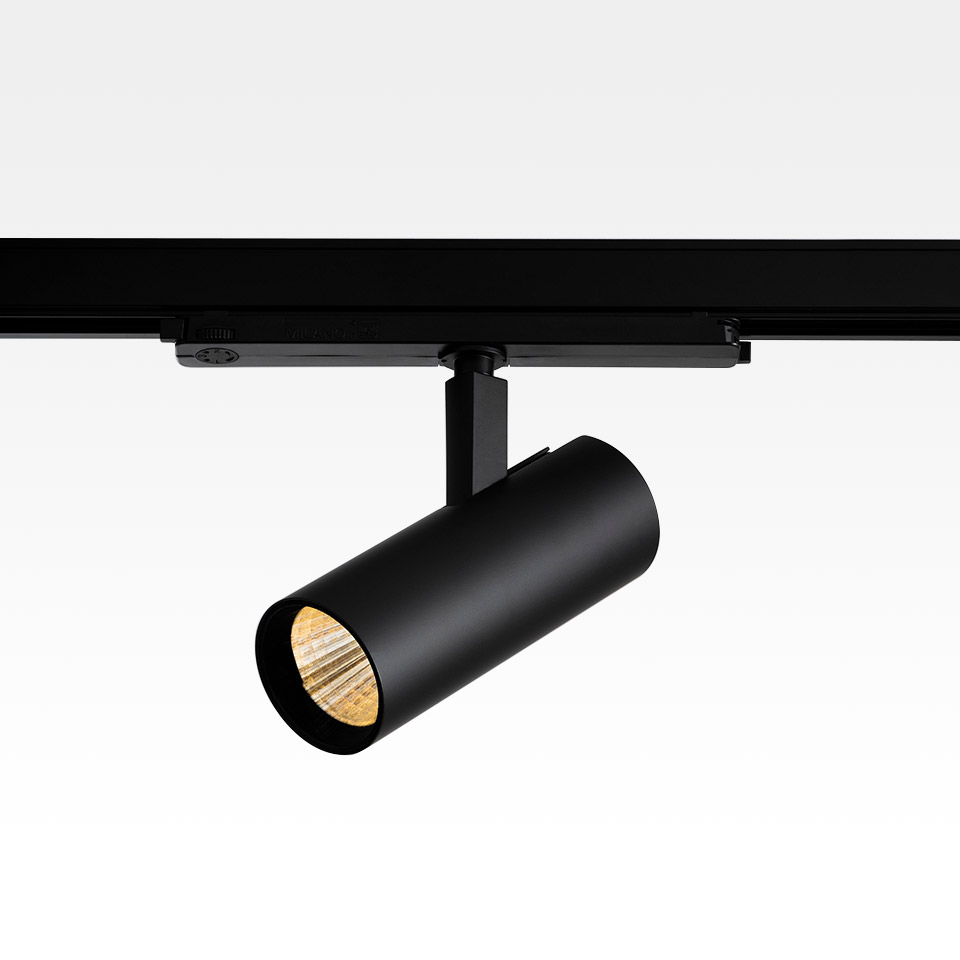 Artemide Vector Track 230V: faretto LED cilindrico nero montato su binario nero, inclinato verso il basso, luce calda visibile