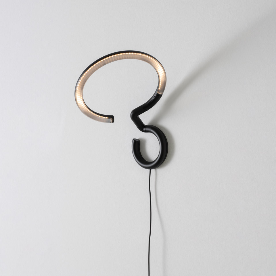 Artemide Vine Light wall lamp: sinuous black tube forming a question-mark shape, upper loop glowing with warm LED light