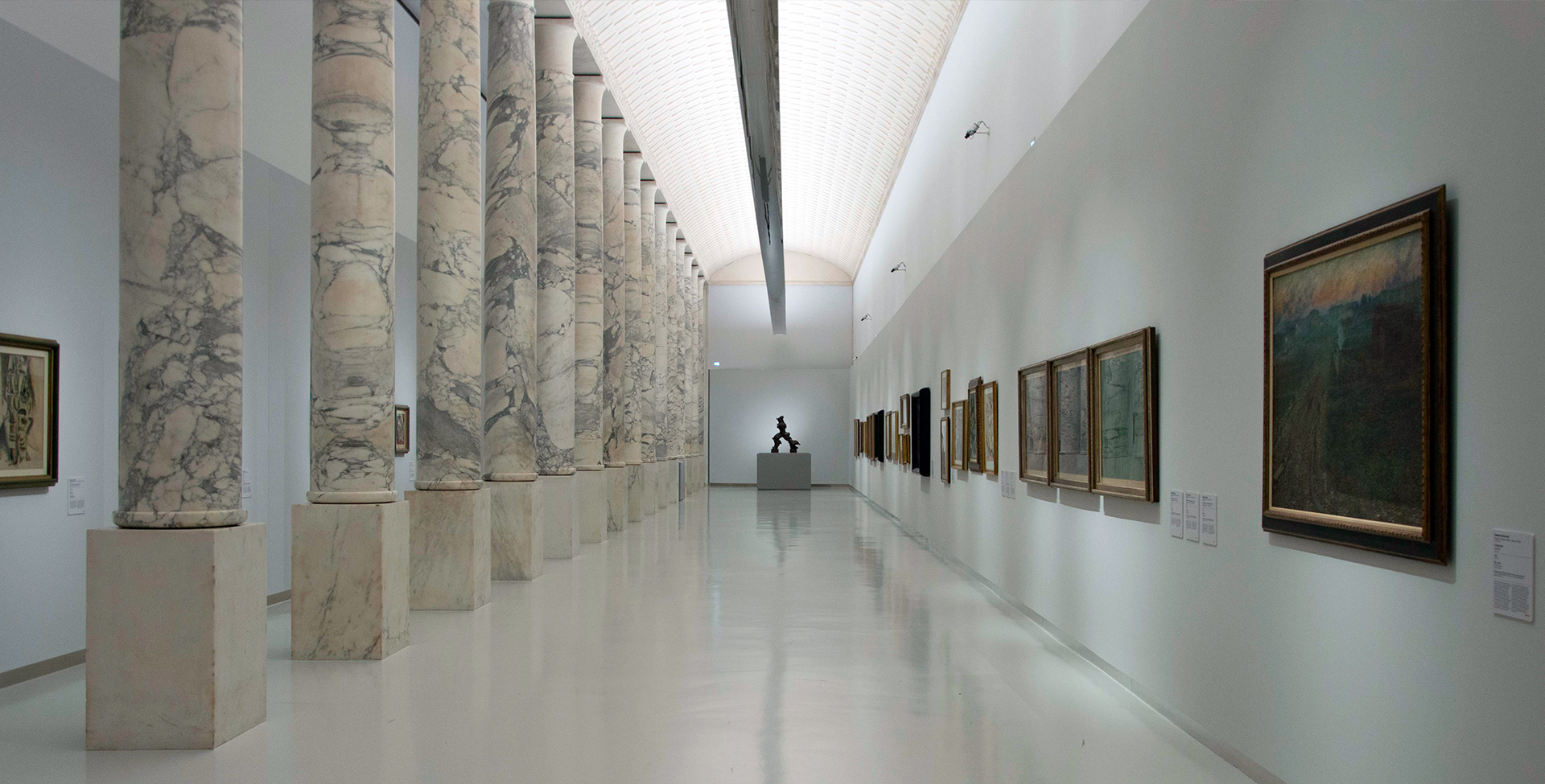 Museum gallery with marble columns, Artemide linear ceiling lights illuminating artwork on white walls and a reflective floor.