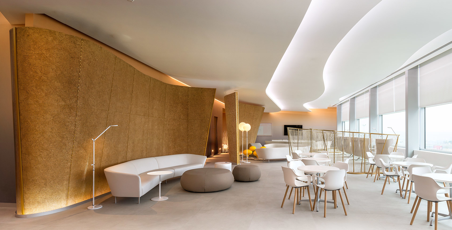 Modern lounge with curved golden wall, white sofas, Artemide floor lamps, and soft indirect ceiling lighting in warm tones