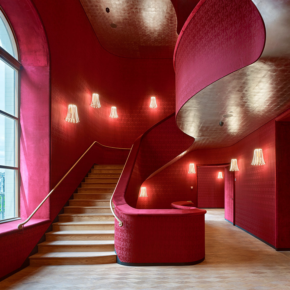 Grand red velvet staircase hall with elegant wall-mounted tassel-shaped pendant lights illuminating the curved spiral stairway.