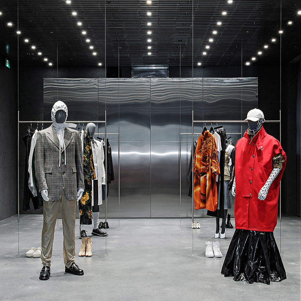 Interno di boutique fashion con faretti a soffitto incassati che illuminano manichini in abiti di design, parete metallica, pavimento in cemento