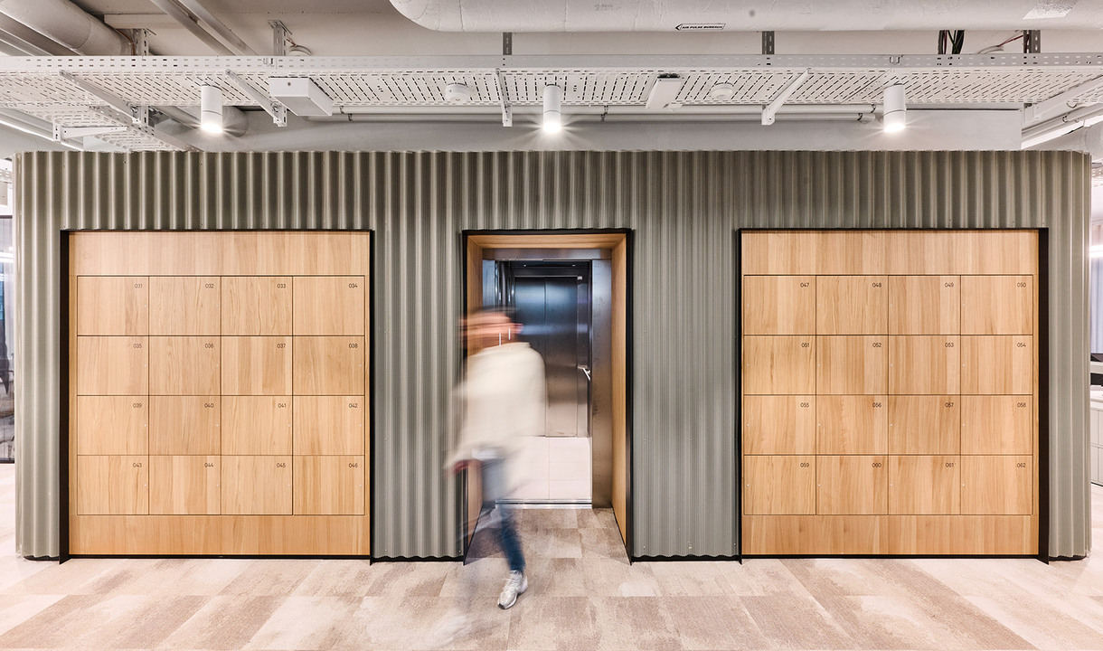 Zona guardaroba con armadietti in legno e ascensore centrale in ambiente aziendale moderno.