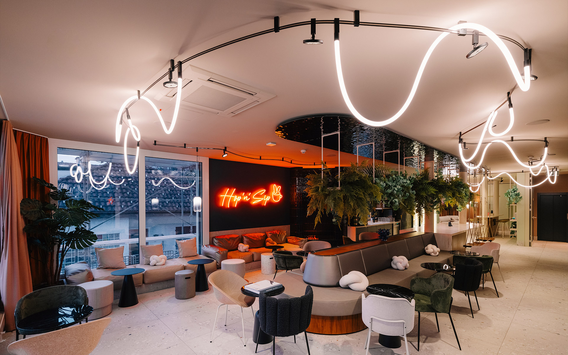 Bar lounge moderno con installazione di tubi LED bianchi sinuosi a soffitto, insegna al neon, piante rigogliose e diverse aree seduta