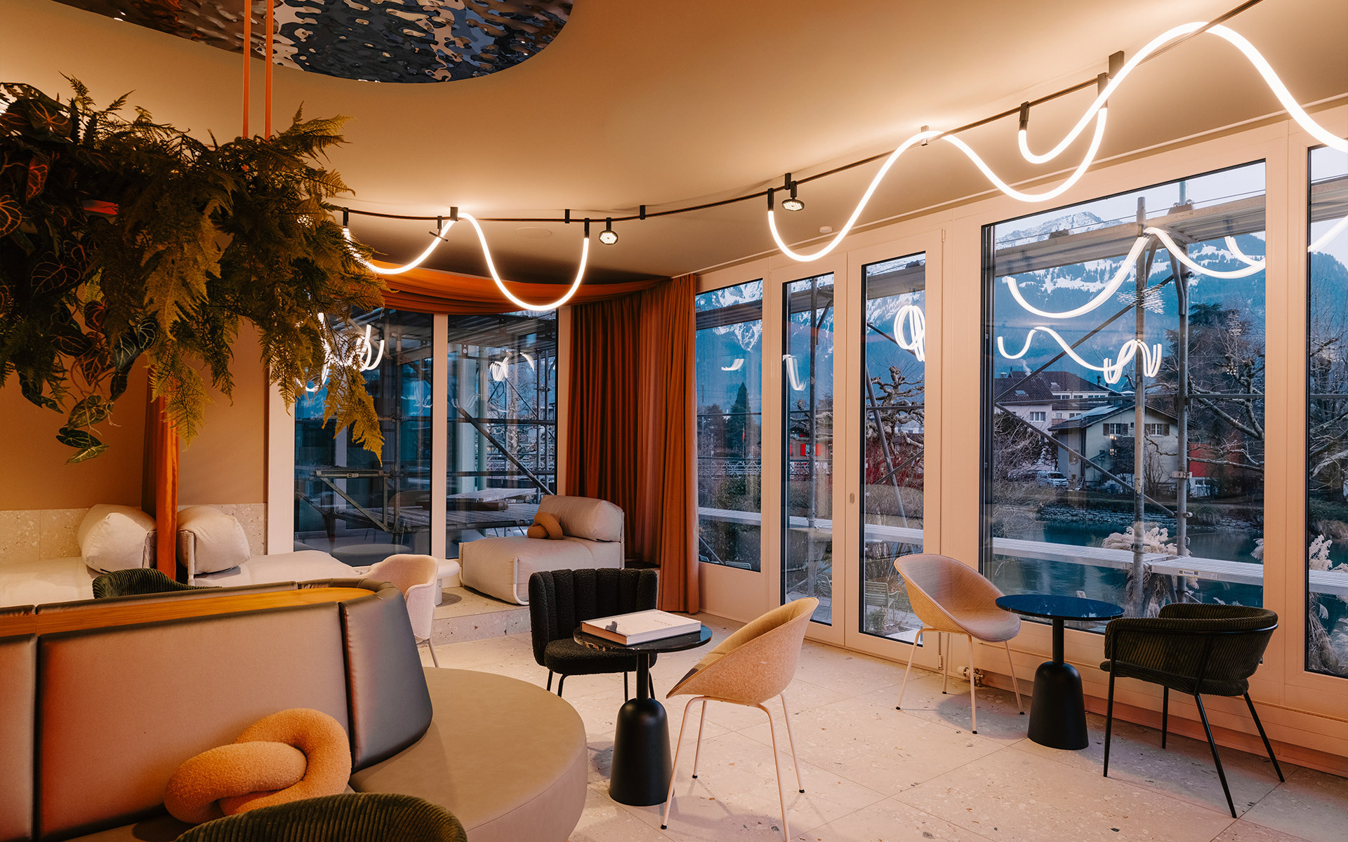 Lounge moderno con illuminazione LED al neon sinuosa bianca e faretti a binario caldi sul soffitto, ampie finestre su una città di montagna.