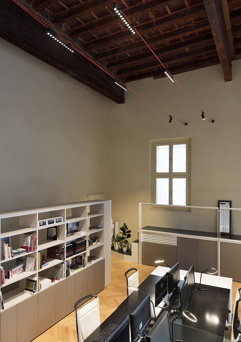 Funivia illumina un ambiente di lavoro con soffitto ligneo storico, librerie, scrivanie e postazioni operative.