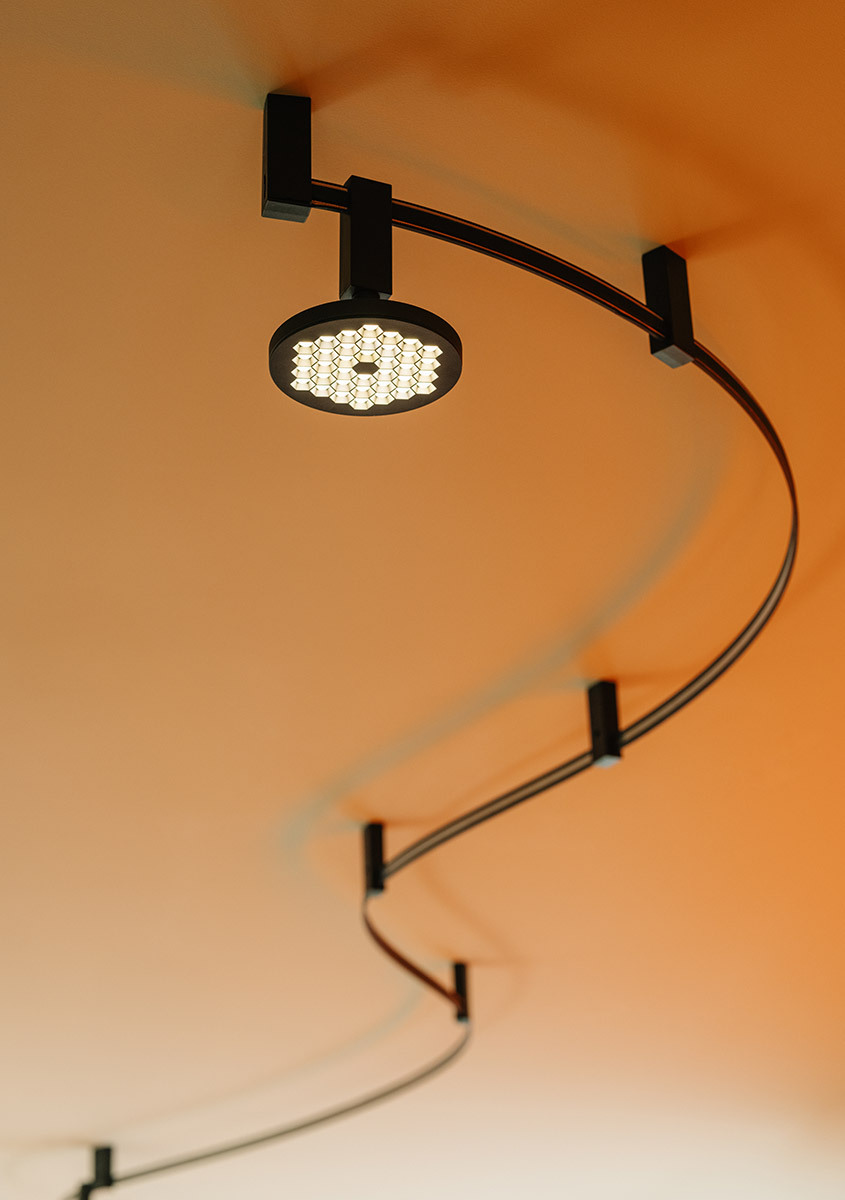Dettaglio del sistema Sylt con binario curvo nero e apparecchio Helgoland acceso su soffitto arancione.