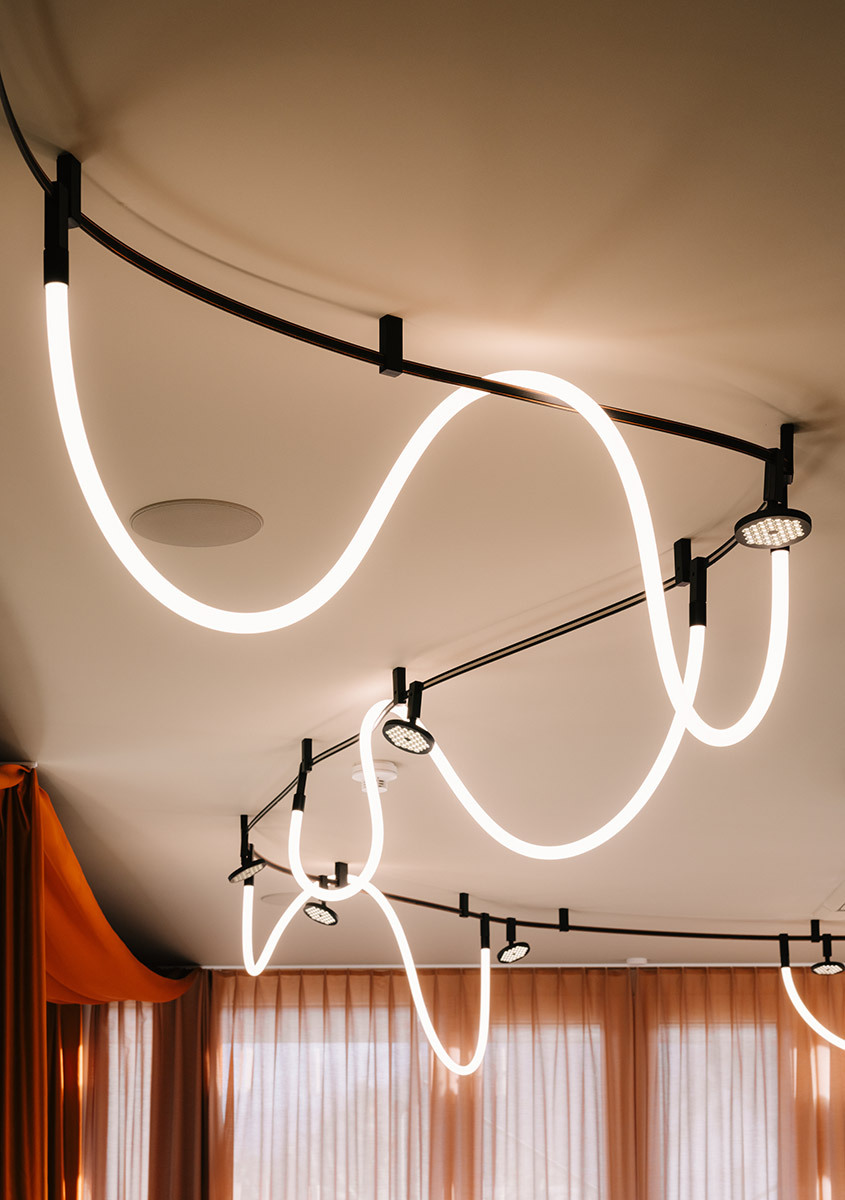 Sistema Sylt a soffitto con binari curvi, faretti e linee luminose in un ambiente lounge.