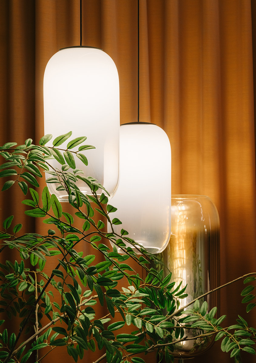 Lampade Gople sospese davanti a tende arancioni, con piante decorative in primo piano.
