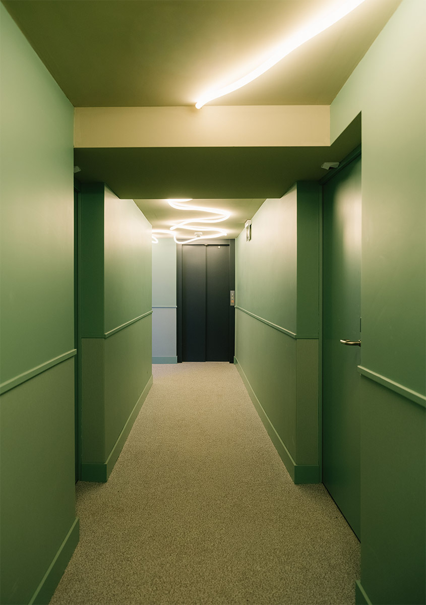 Corridoio verde con La Linea a soffitto e porte scure sullo sfondo.