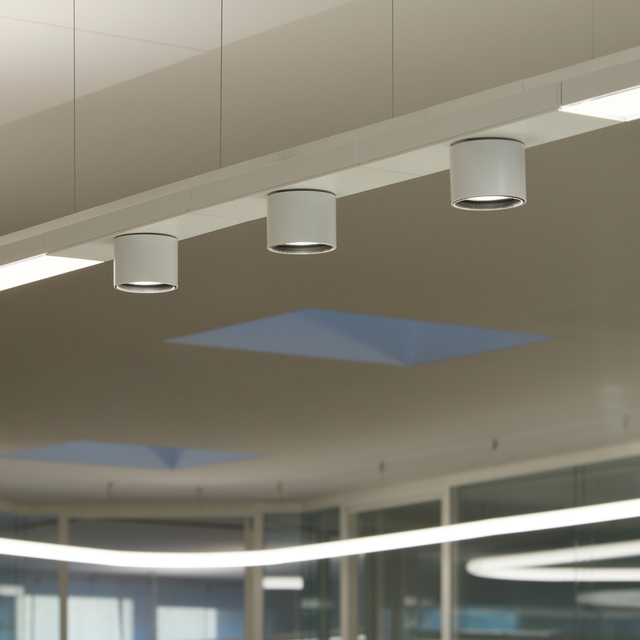 Dettaglio del sistema di illuminazione a soffitto Hoy System con faretti cilindrici bianchi orientabili.