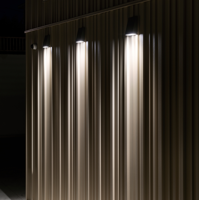 Dettaglio di illuminazione esterna sulla facciata della nuova sede direzionale Fornaroli Polymers con lampade Cuneo a parete che proiettano fasci di luce verticali.