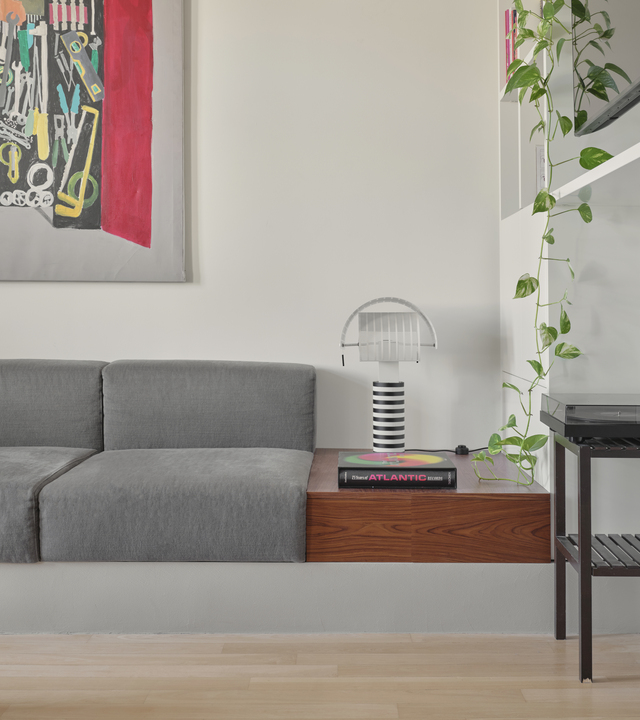 Lampada da tavolo Shogun di Artemide su piano in legno nella zona living, accanto al divano grigio e alla libreria bianca.