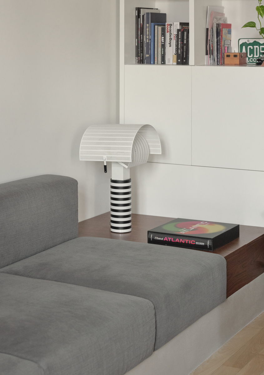 Primo piano della lampada da tavolo Shogun di Artemide nella zona living, appoggiata su un piano in legno accanto al divano.