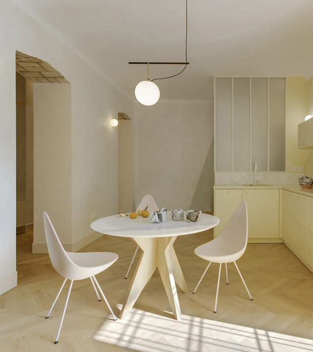 Zona pranzo con tavolo rotondo, sedie bianche e lampada a sospensione in un interno dai toni chiari e minimali.