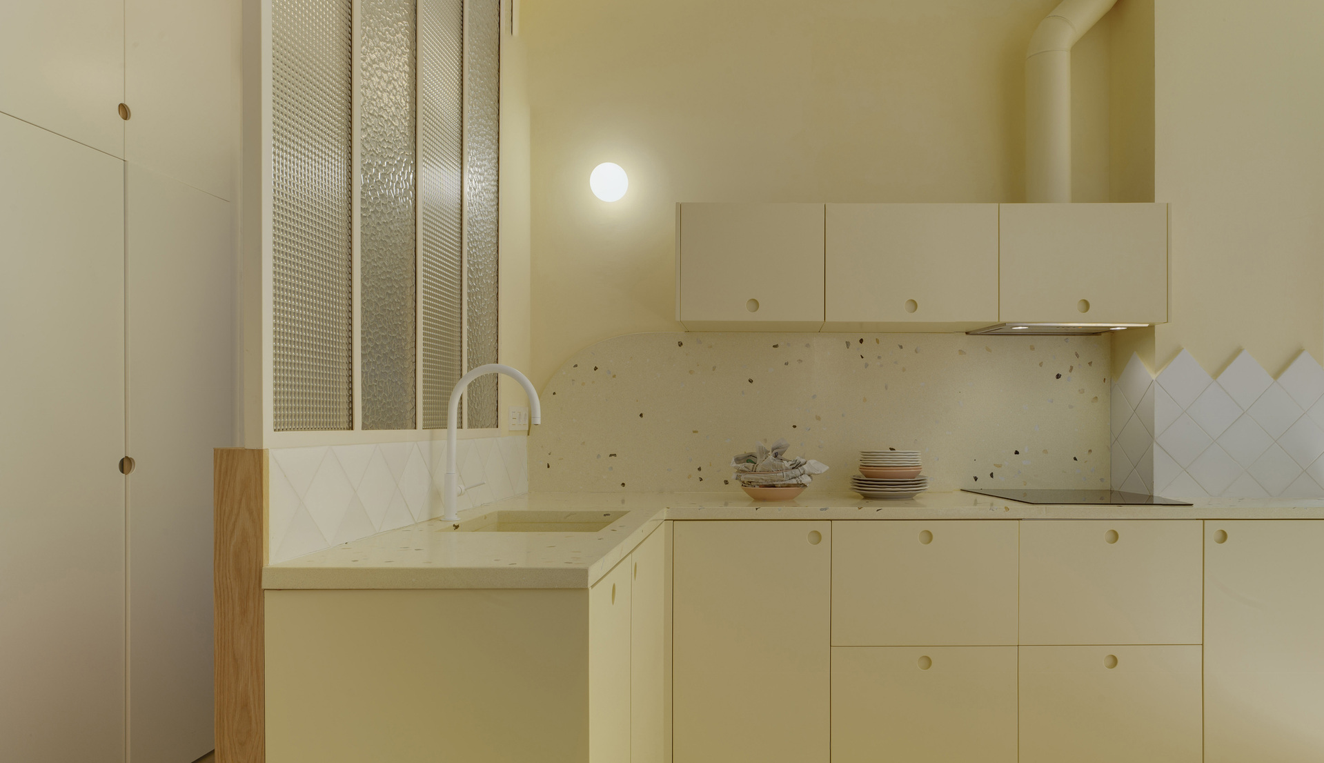 Dettaglio della cucina con mobili color crema vetrata strutturata e applique a parete.