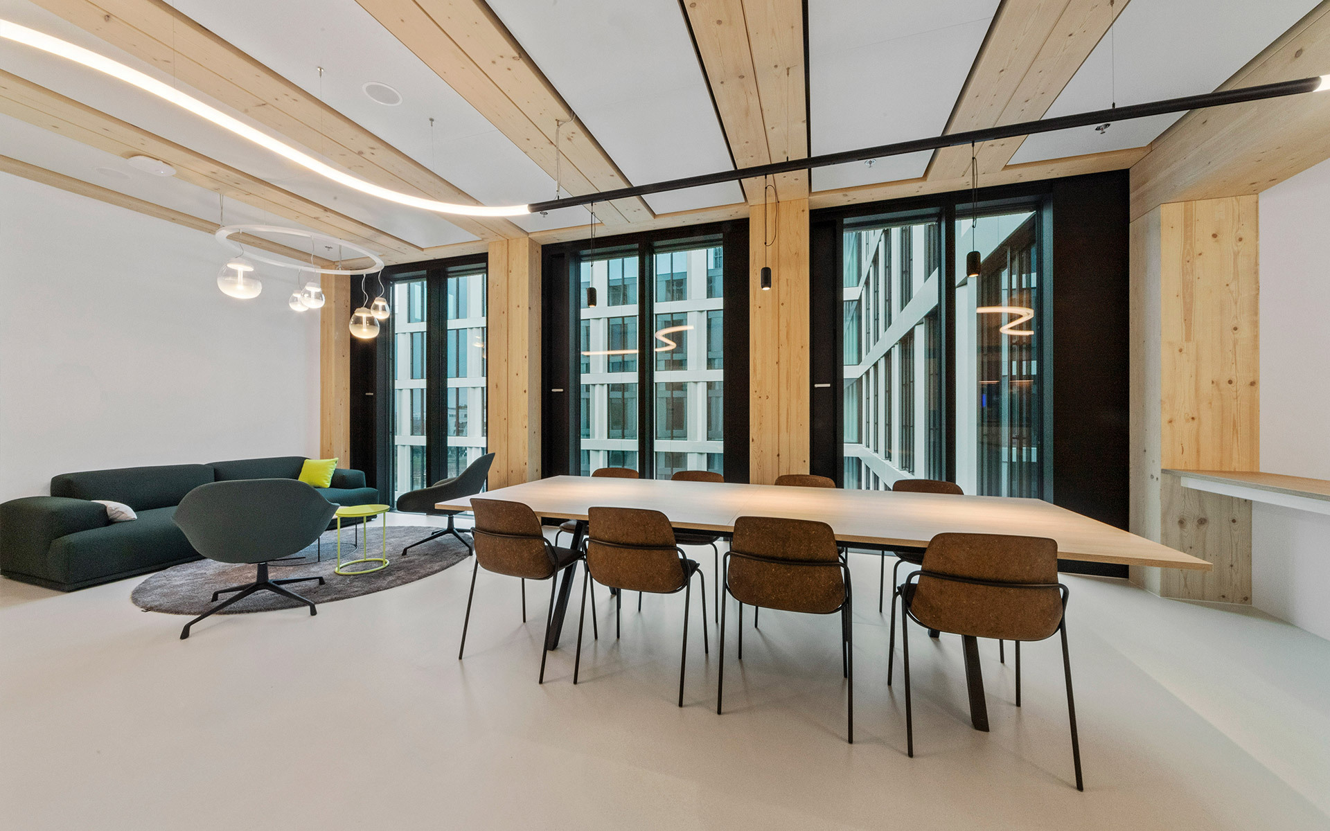 Modern meeting room with Artemide pendant lights, long wooden table, brown chairs, lounge area, and floor-to-ceiling windows with natural light