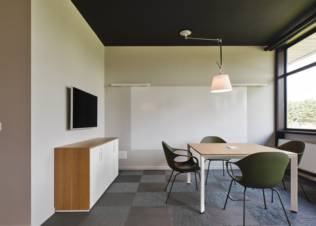 Modern meeting room with Artemide Tolomeo pendant lamp over a wooden table, green chairs, whiteboard, and dark ceiling.