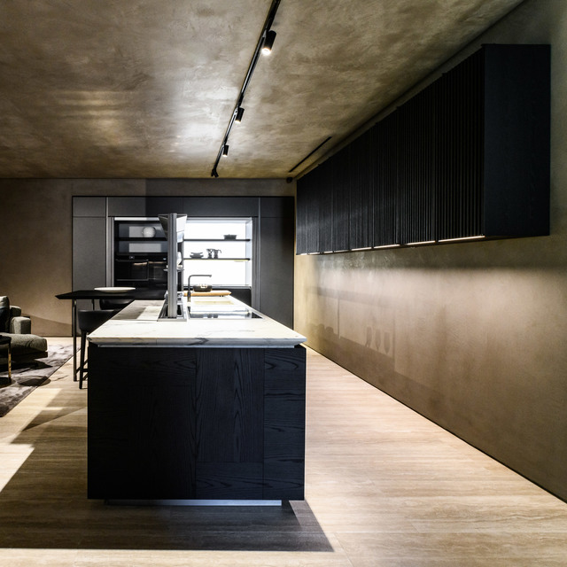 Modern dark kitchen with island, marble countertop, black cabinetry, and track spotlights mounted on concrete ceiling.