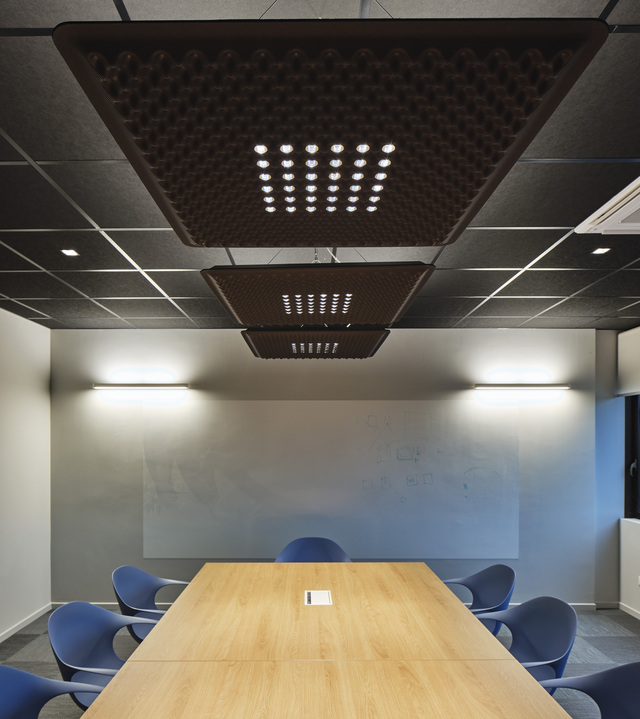 Conference room with two Artemide ceiling panels featuring LED dot arrays, illuminating a wooden meeting table surrounded by blue chairs.