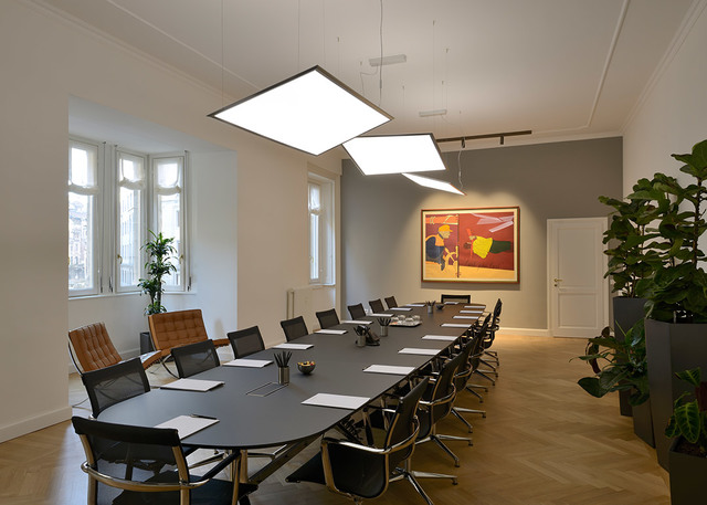 Conference room with large dark table, mesh chairs, and two square LED pendant lights illuminating the space above.