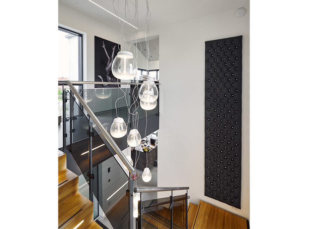 Gruppo di lampade a sospensione Artemide Muse con diffusori in vetro sopra una scala moderna con ringhiera in vetro e gradini in legno.