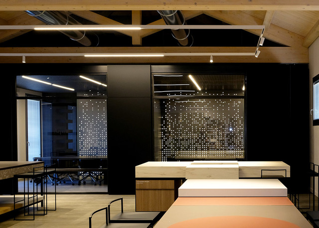 Modern office interior with Artemide linear LED ceiling lights illuminating wooden workstations against a dark perforated panel backdrop