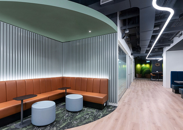 Lounge ufficio moderno con sedute curve in pelle arancione, pannelli a parete illuminati e luci lineari LED a soffitto a zigzag nel corridoio.