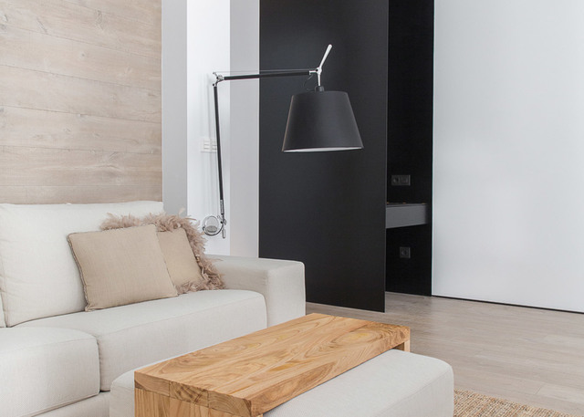 Lampada da parete Artemide Tolomeo Mega con paralume nero su braccio regolabile, che illumina un soggiorno moderno con divano bianco e tavolino in legno