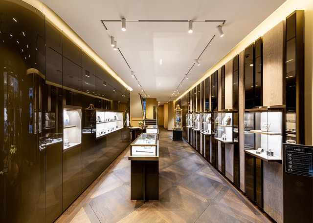 Luxury jewelry store interior with track spotlights illuminating display cases along dark wood-paneled walls and central counters.