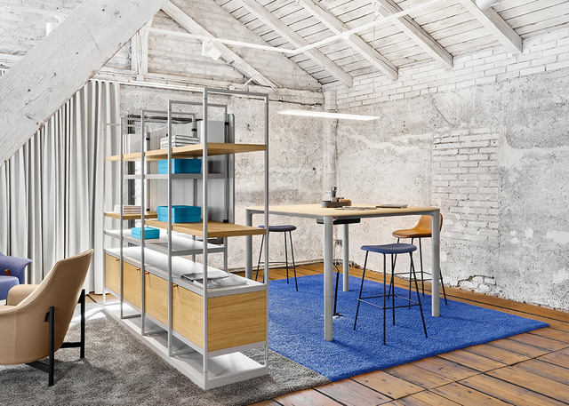 Spazio di lavoro moderno con lampada a sospensione lineare Artemide sopra una scrivania alta, libreria modulare, tappeto blu e pareti in mattoni a vista