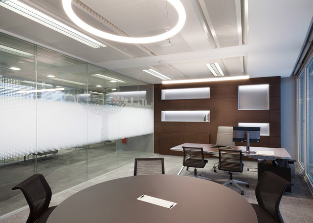 Ufficio moderno con lampada a sospensione circolare LED Artemide a soffitto, che illumina un tavolo riunioni e un'area scrivania direzionale.