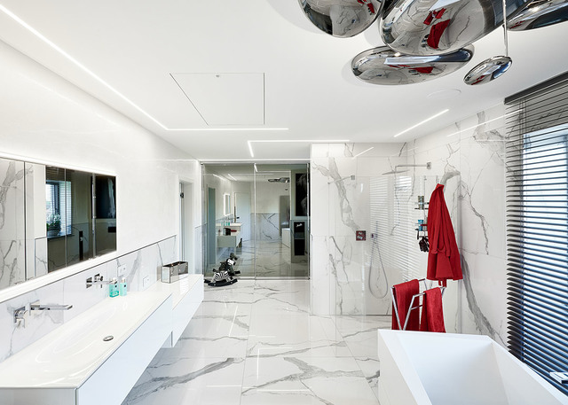 Lussuoso bagno in marmo con illuminazione LED lineare a incasso sul soffitto e lampade a sospensione cromate sopra una vasca freestanding