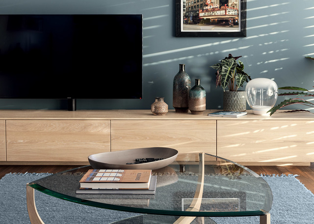 Soggiorno moderno con tavolino in vetro, mobile TV in legno chiaro, vasi decorativi e lampada da tavolo sferica in vetro sul credenzino
