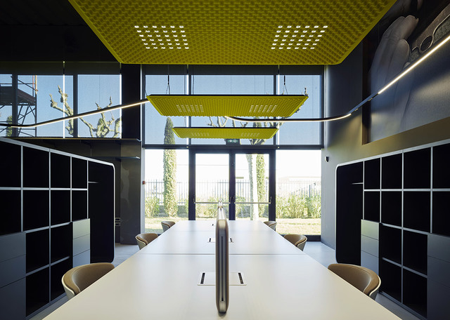 Modern conference room with long white table, black shelving, and yellow perforated acoustic ceiling panels doubling as pendant lights