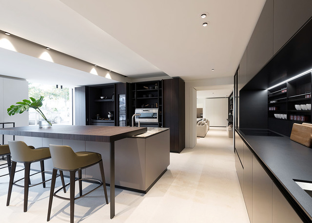 Cucina moderna con faretti da incasso a soffitto, mobili scuri, isola con sgabelli da bar e illuminazione LED sottopensile.