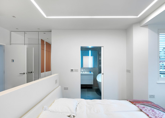 Camera da letto moderna bianca con illuminazione LED a cornice incassata nel perimetro del soffitto, che illumina dolcemente la stanza sopra un letto matrimoniale.