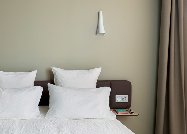 Lampada da parete conica bianca Artemide montata sopra la testiera di un letto in una camera minimalista con pareti verde salvia.