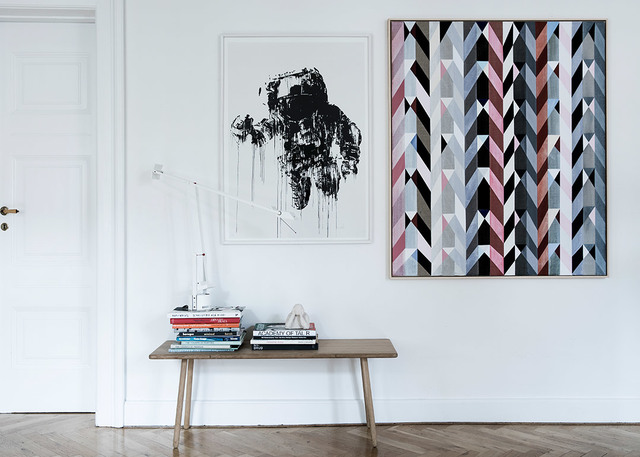 Minimalist interior with a white articulated desk lamp on a wooden bench, flanked by abstract artwork on white walls.