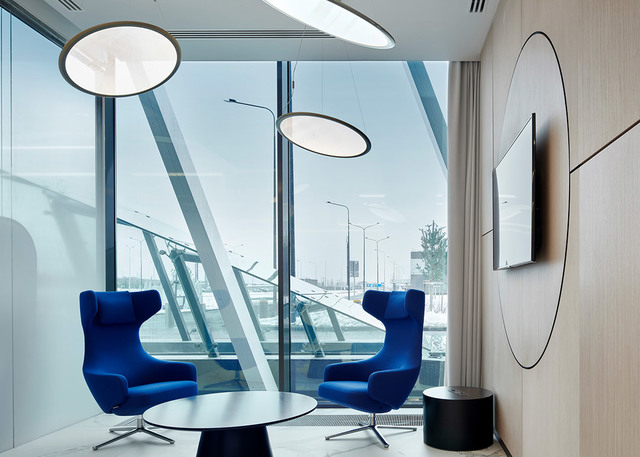Lounge moderna con due sospensioni circolari Artemide Alphabet of Light sopra poltrone blu, finestre a tutta altezza e cerchio decorativo a parete.