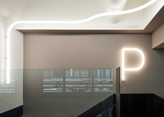 Spazio interno con striscia LED bianca sinuosa sul soffitto e lettera P luminosa su parete beige sopra una partizione in vetro