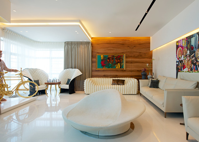 Soggiorno moderno con illuminazione a cornice, faretti a soffitto, mobili scultorei bianchi, parete in legno e opere d'arte colorate.