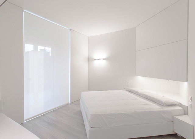 Minimalist all-white bedroom with a wall-mounted Artemide sconce above the bed headboard providing soft ambient lighting