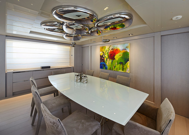 Sala da pranzo moderna con plafoniera scultorea a bolle cromate sopra un tavolo in vetro bianco circondato da sedie imbottite grigie