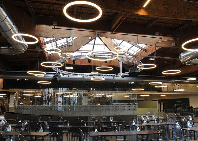 Restaurant interior with multiple Artemide Alphabet of Light circular LED pendant rings suspended at varying heights from an industrial ceiling.