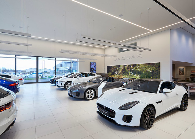 Jaguar car showroom with linear pendant lighting illuminating a row of luxury vehicles on white tile floor