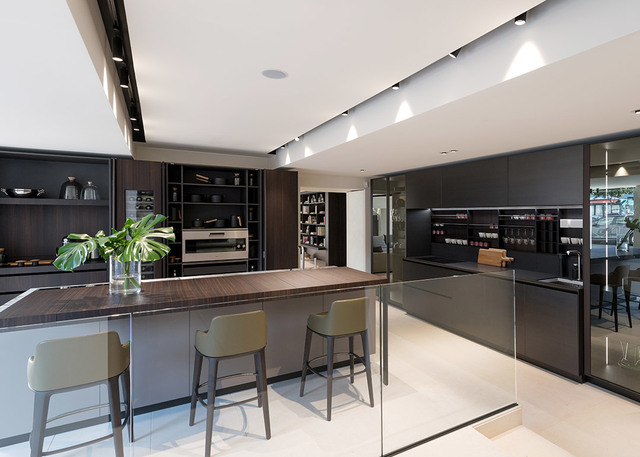 Cucina moderna con mobili scuri illuminata da faretti da incasso Artemide su binario a soffitto, con isola in legno e sgabelli verdi